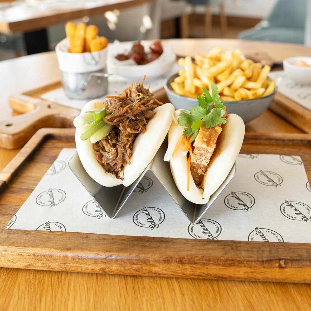 Bao buns on a wooden board with fries and a seafood roll on a table at Saltwater
